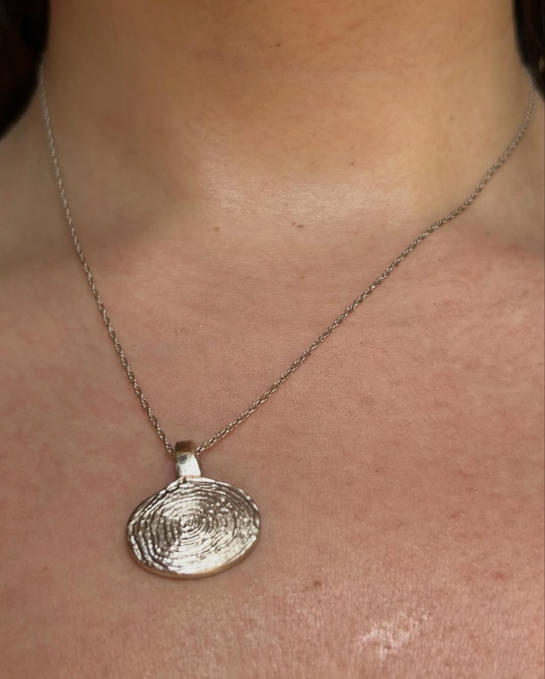 A textured topographic silver pendant worn on a fine chain