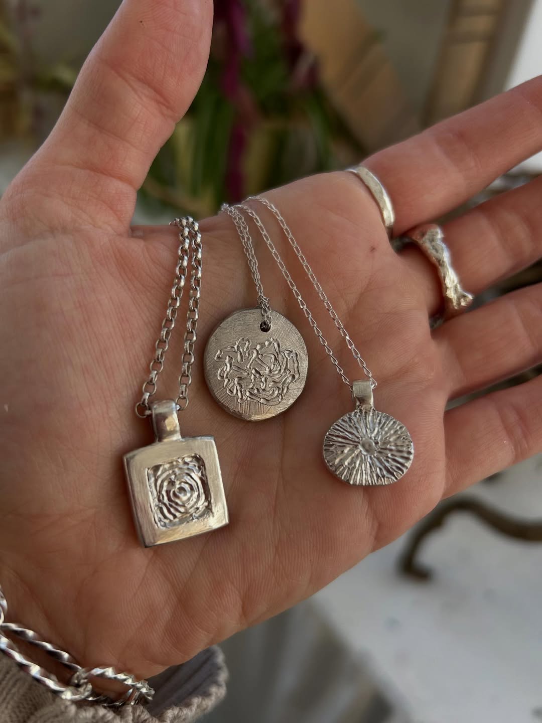 Three hand-cast silver pendants resting in an open palm