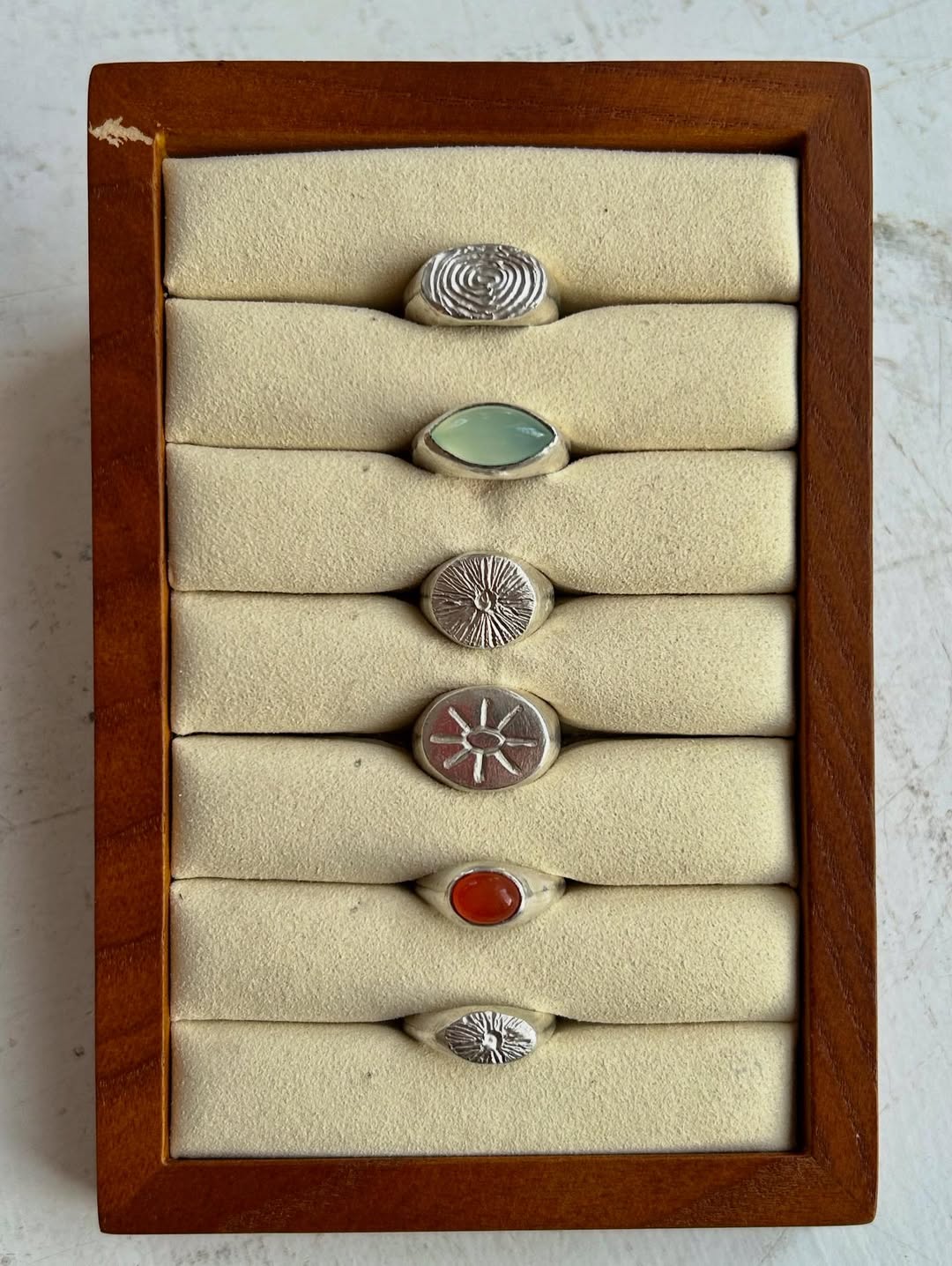 Six sculptural silver rings displayed in a wooden ring box, including carnelian and chalcedony stones
